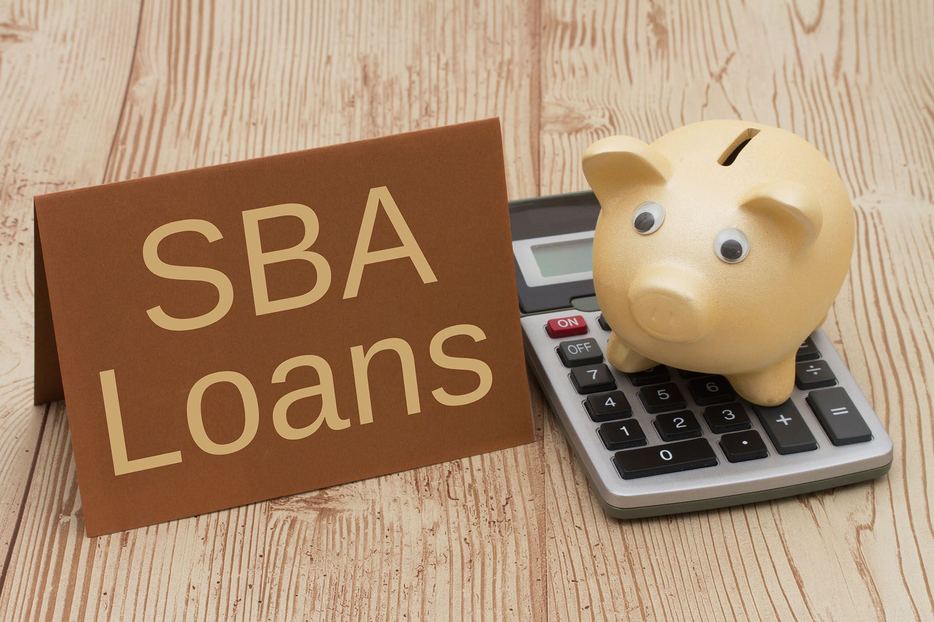 SBA loan sign next to a piggy bank on a calculator